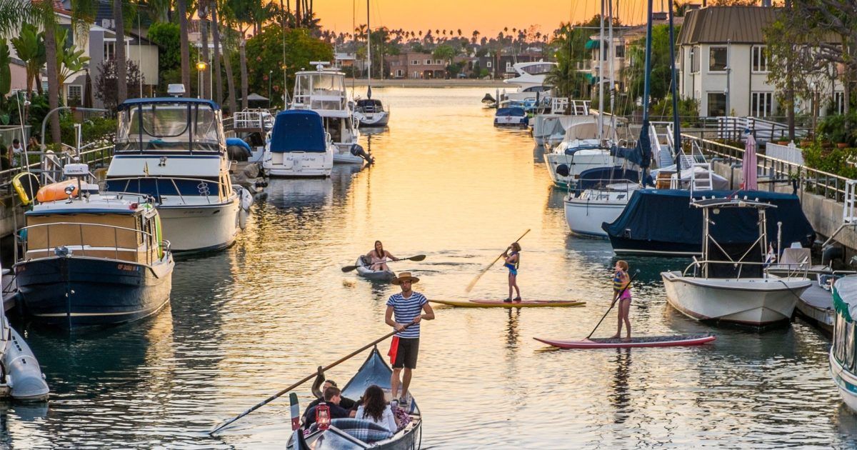 Paddleboarders and a gondola in the Naples canals near Alamitos Bay Marina at sunset in Long Beach