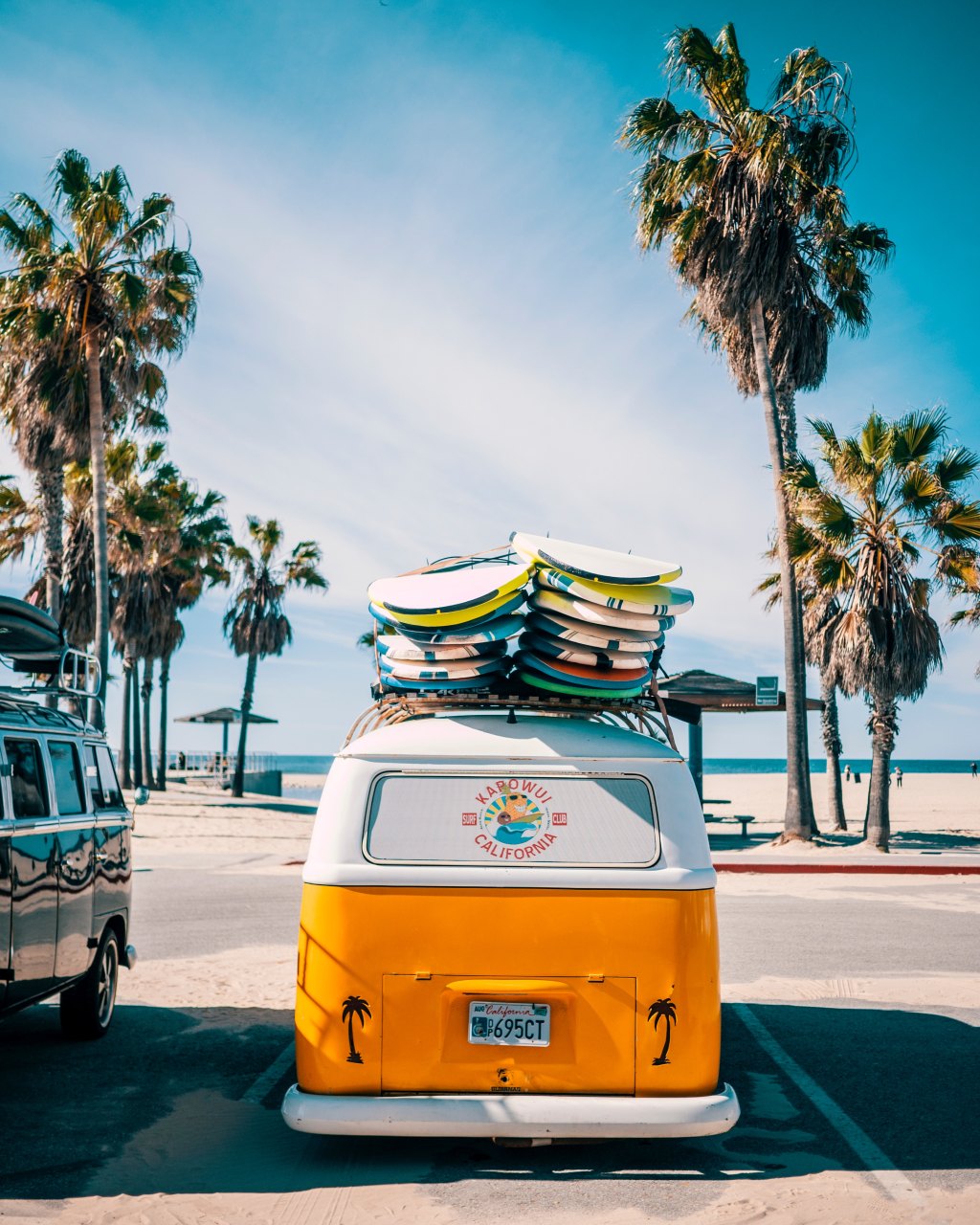 Yellow surf van loaded with surfboards parked by palm trees at Venice Beach