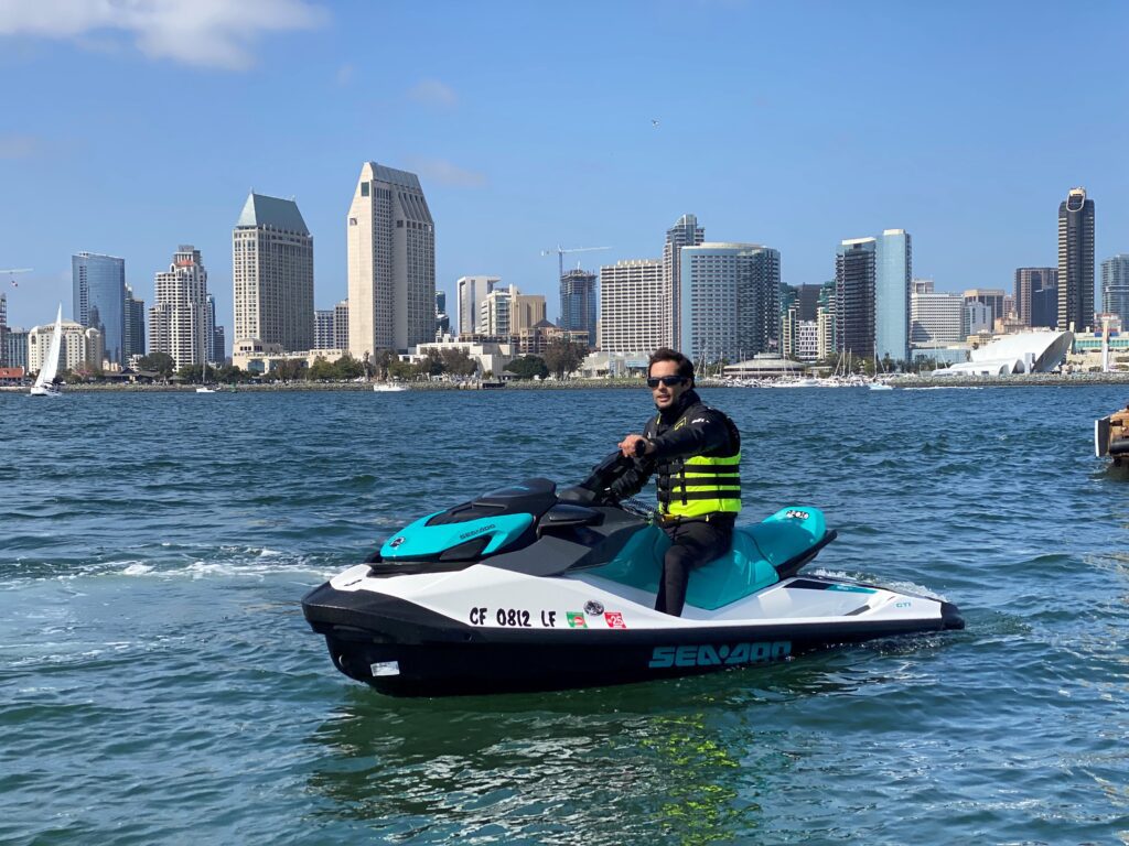 A rider on a jet ski or wave runner in San Diego Bay with the downtown San Diego skyline behind him